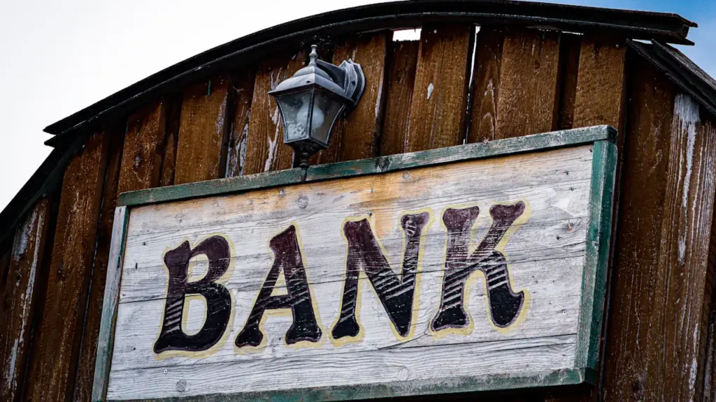 A rustic wooden sign reading Bank mounted on a dark timber building wall.