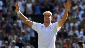 A tennis player in a white shirt and cap waving to a large crowd.