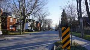 A quiet suburban street with a yellow and black traffic hazard sign.