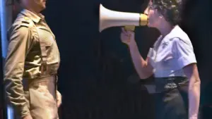 A woman speaks into a megaphone at a man in military-style vintage clothing.