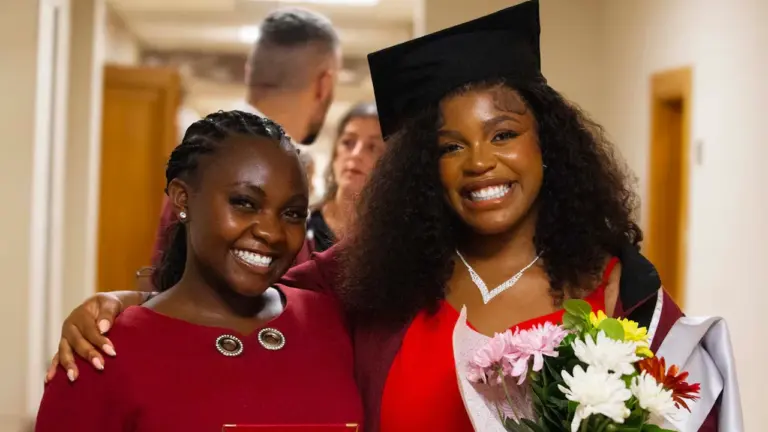 Two women celebrating a graduation achievement with flowers and an award plaque.