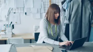 A female designer working on her laptop in a bright professional tailor studio.