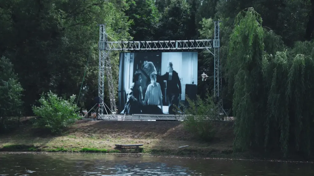 Large outdoor cinema screen set up in a park by the water.