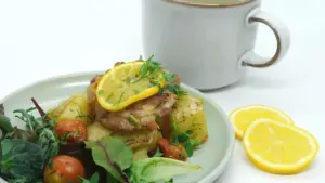 A fresh warm potato and fish salad served with lemon on a plate.