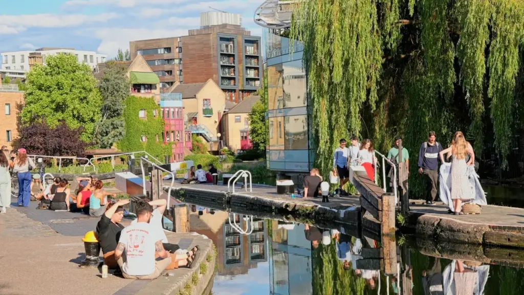 People enjoy a sunny afternoon sitting along the banks of a calm city canal.