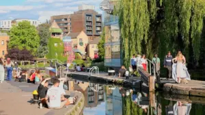 People enjoy a sunny afternoon sitting along the banks of a calm city canal.