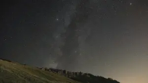 Starry night sky above a dark grassy hill in the countryside