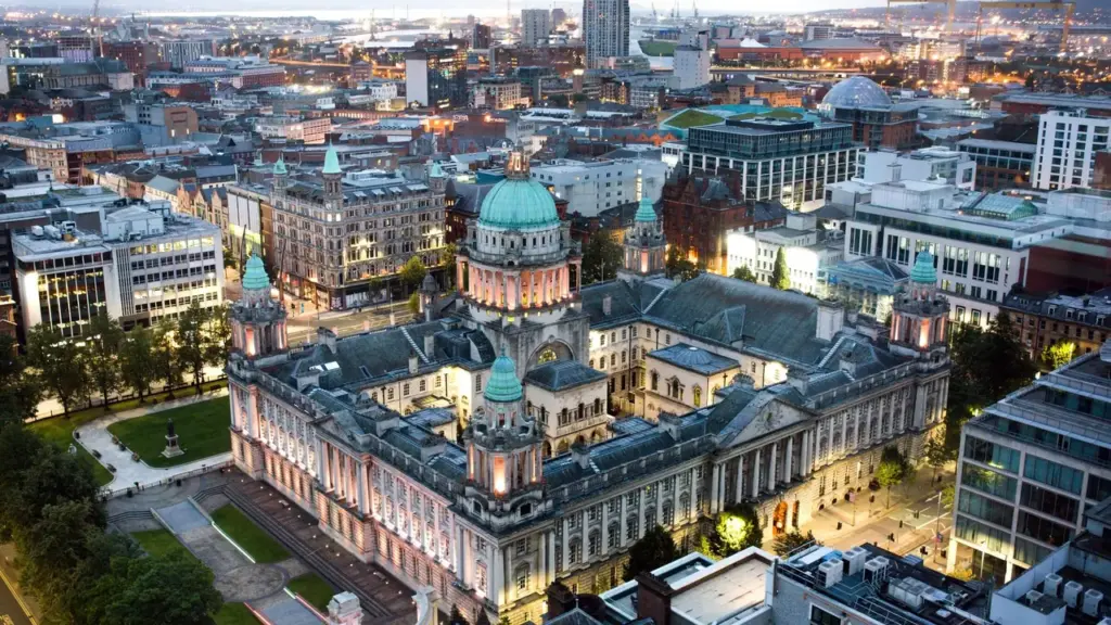Aerial view of Belfast City Hall at twilight surrounded by the illuminated city center.