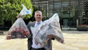 A man in a suit holding two large plastic bags filled with counterfeit toys.