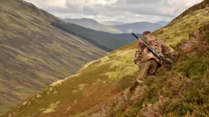 A hunter walks through the vast, rugged Scottish moorland landscape during the shooting season.