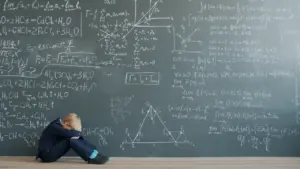 A student sits on the floor overwhelmed by complex math equations on a blackboard.