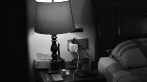 Grayscale photograph of a bedside lamp and nightstand, capturing a peaceful, organized atmosphere.