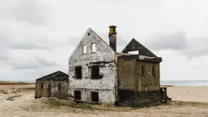 An abandoned concrete house standing on a desolate coast under a cloudy sky.