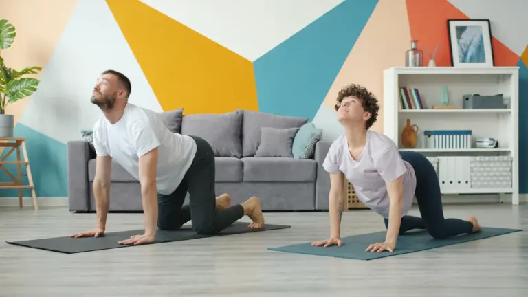 A man and woman practicing the cow yoga pose in a modern living room.
