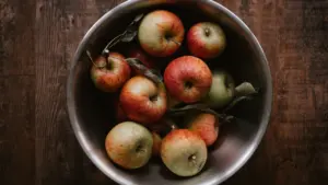A metal bowl filled with fresh red apples on wooden surface.
