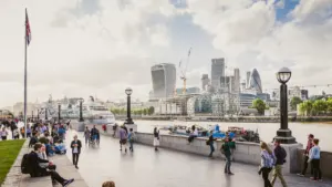 People walking along the River Thames with London city skyline in the background.