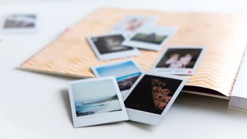 Close-up of assorted polaroid style family photographs scattered on a white wooden table surface.