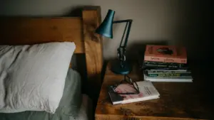 Books and glasses on a bedside table in a moody, quiet bedroom setting.
