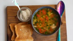 Bowl of vegetable soup with toast served on a wooden board