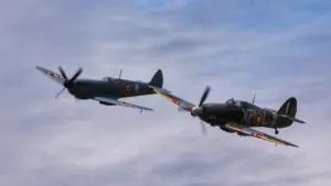 A historic Spitfire and Hurricane flying in formation against a cloudy sky.