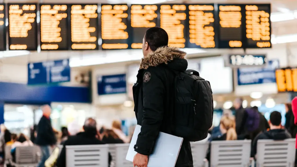 A passenger checking a large flight information display board at a UK airport.