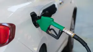 Green fuel pump nozzle refuelling a white car at a petrol station.