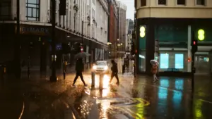 People with umbrellas walking across a rainy Manchester street in autumn.