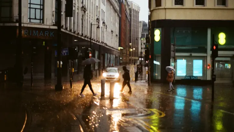 People with umbrellas walking across a rainy Manchester street in autumn.