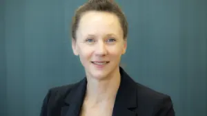 A woman with light brown hair pulled back wearing a professional black blazer jacket.