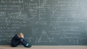 A young student sitting on the floor against a chalkboard filled with complex equations.
