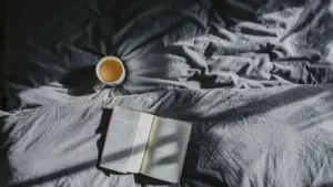 A warm cup of tea beside an open book on a cozy gray textile.