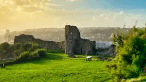 Ancient stone castle ruins set in a peaceful grassy English landscape at sunset.