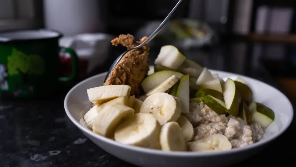 Bowl of creamy porridge topped with fresh pear slices and cinnamon on a dark surface.