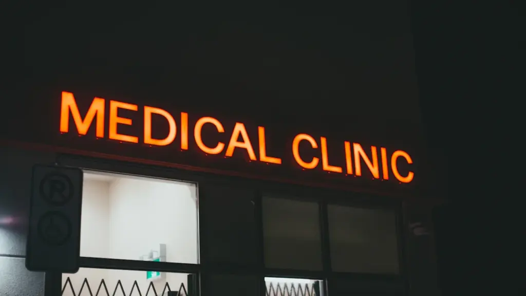 Glowing orange sign for a medical clinic at night on a dark street.